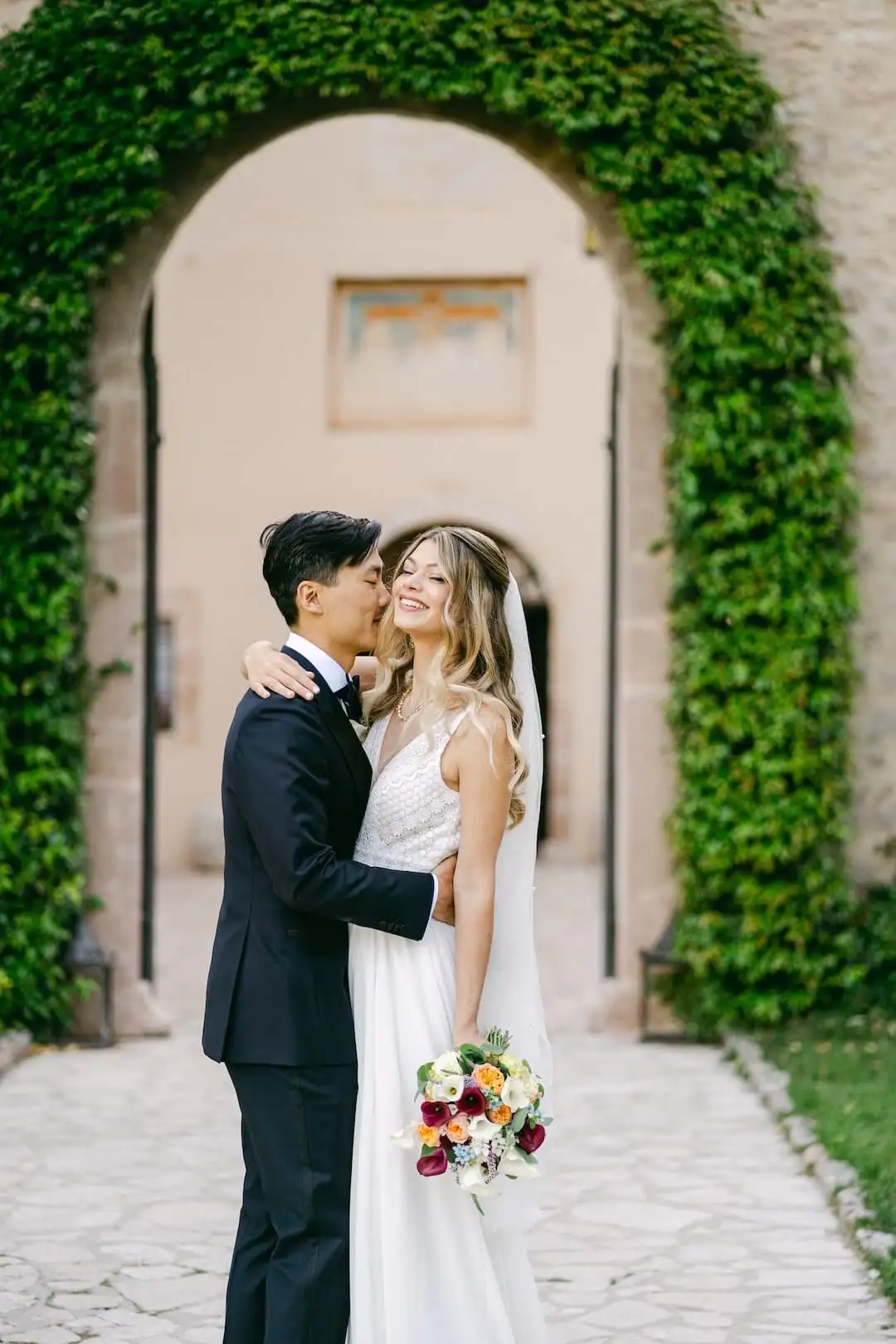 Bride and groom embracing under an ivy-covered archway at a historic Italian villa