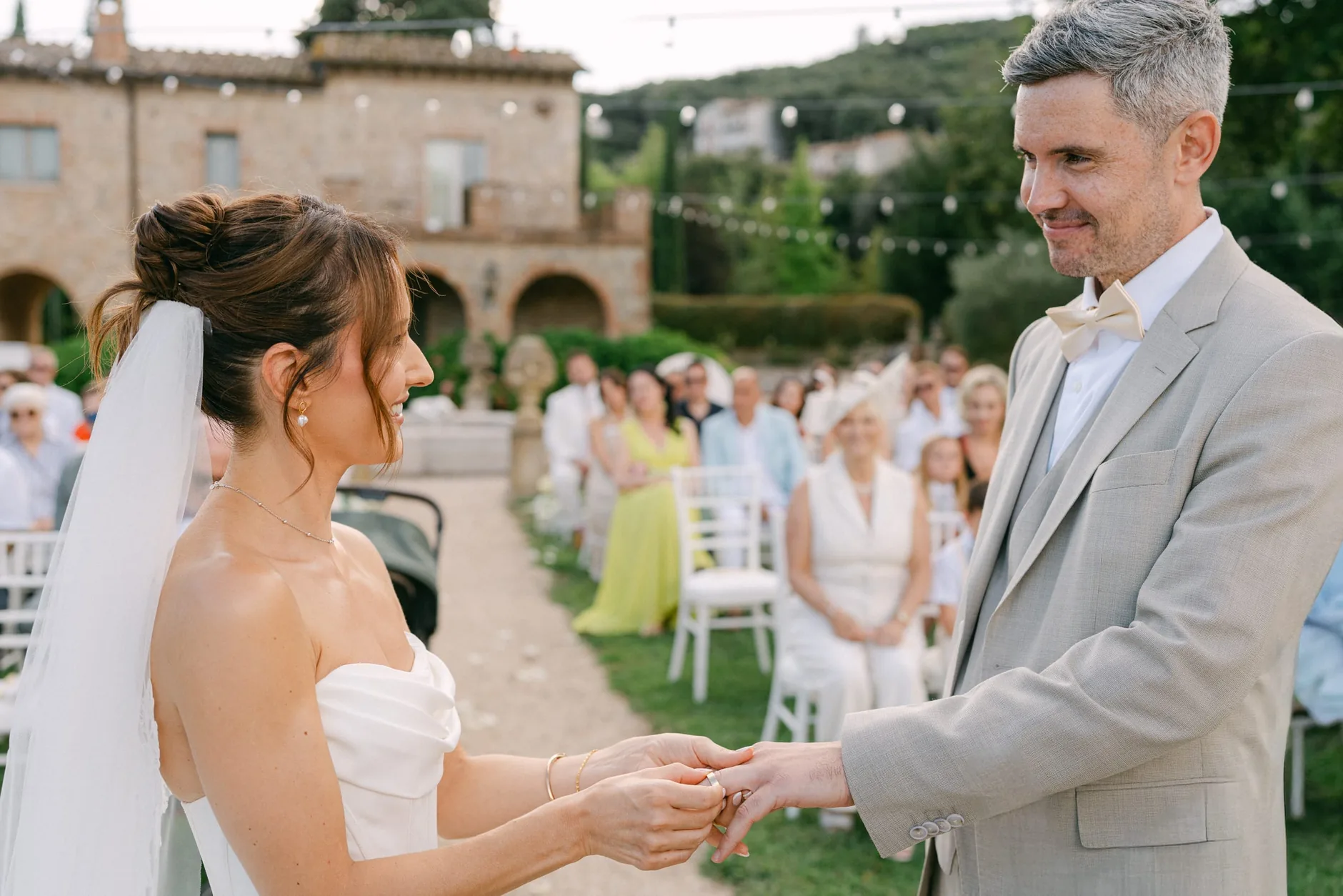 Christina ed Emilio mano nella mano durante le promesse, con la villa e gli invitati alle spalle