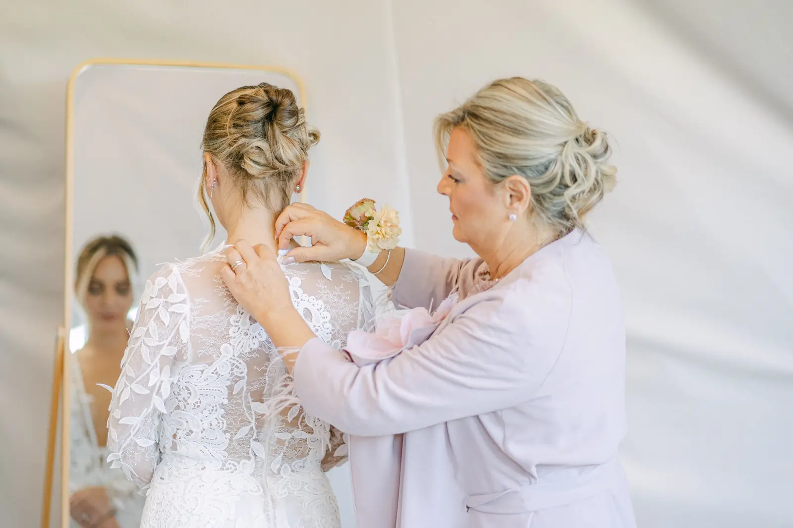 La sposa aiutata a indossare l’abito davanti allo specchio