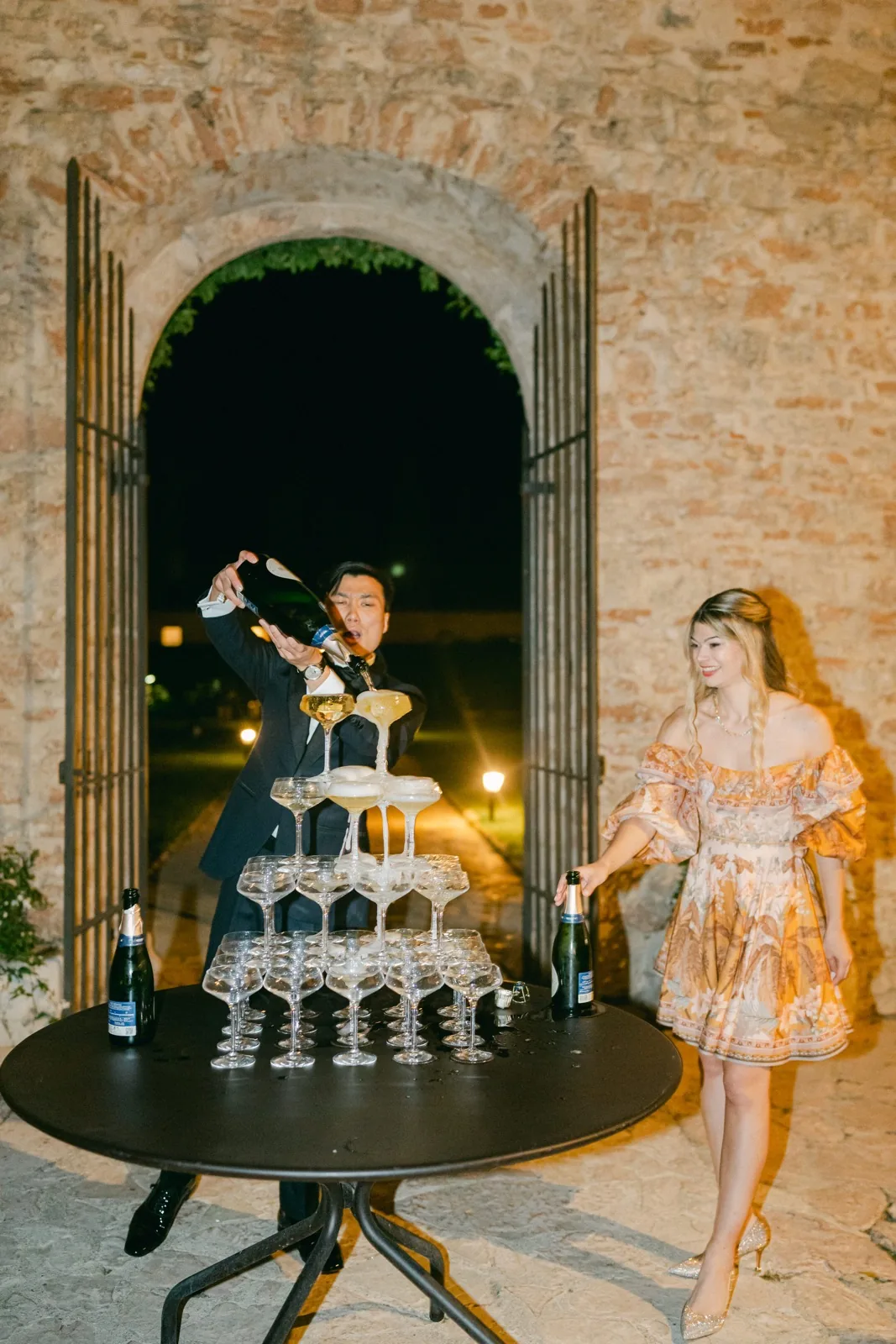 Gli sposi versano lo champagne sulla torre di coppe, sotto l’arco di pietra